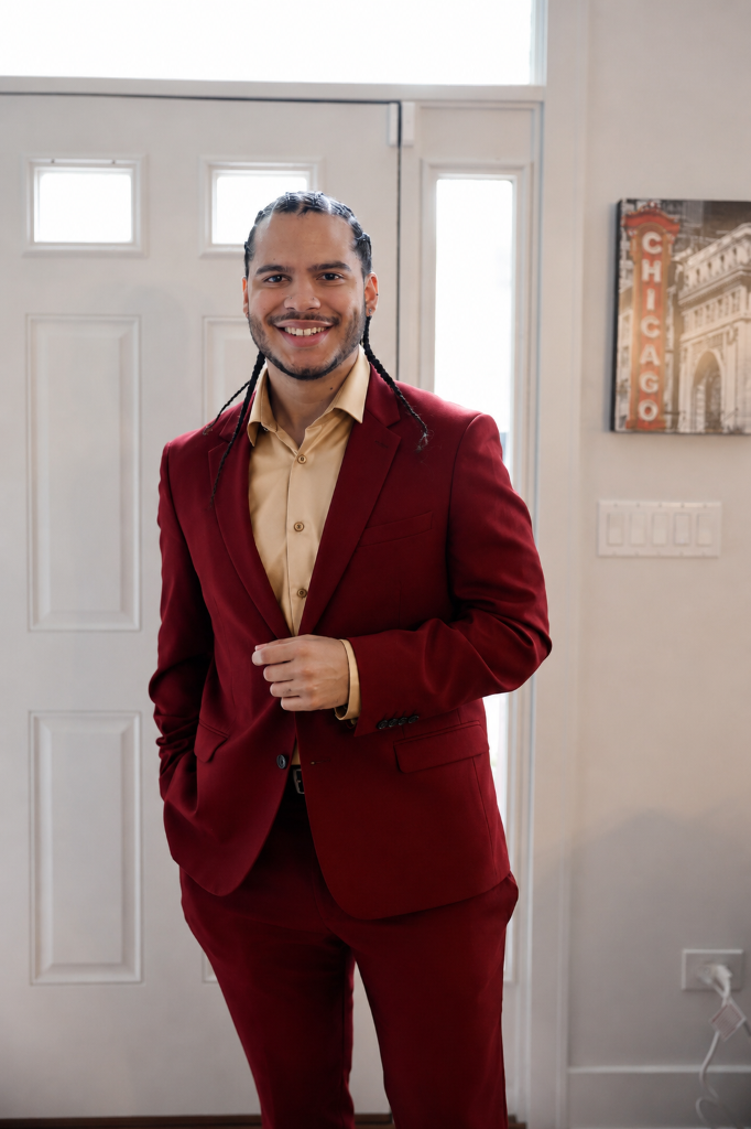 Joshua H. Jimenez smiling, wearing a ruby red suit with a gold dress shirt.